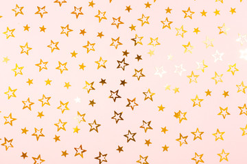 Festive background. Golden confetti stars on pink paper.