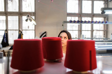 close up photo of a young woman looking at red threads in cones on the knitting machine