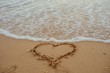 close up photo of a heart drawn on the sand of a beach with wave and sunlight