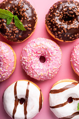 Overhead shoot of colorful donuts on pink background with mint. Birthday party food concept. Top view