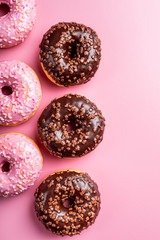 Overhead shoot of colorful donuts on pink background with mint. Birthday party food concept with copy space. Top view