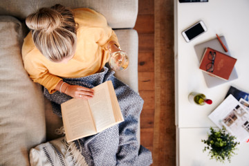Overhead Shot Looking Down On Woman At Home Lying On Reading Book And Drinking Wine