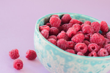 Close up view on ripe fresh raspberry bowl on the pink background