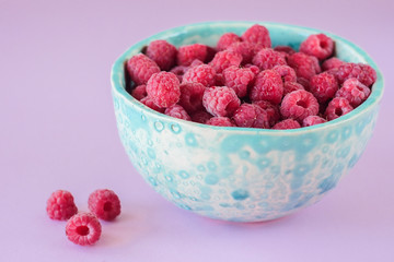 Close up view on ripe fresh raspberry bowl on the pink background