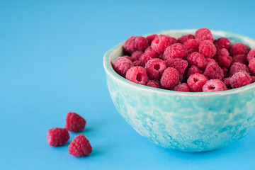 Close up view on ripe fresh raspberry bowl on the blue background
