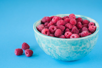 Close up view on ripe fresh raspberry bowl on the blue background