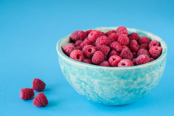 Close up view on ripe fresh raspberry bowl on the blue background