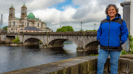 Beautiful mature Mexican woman smiling with blue jacket with the bridge over the river Shannon in...