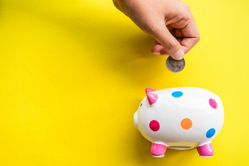 hand of someone insert coin to piggy bank with yellow paper background 