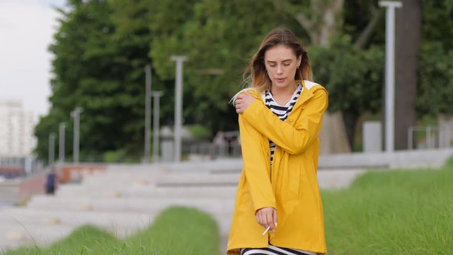 Pretty young girl in yellow rain coat smoking cigarette enjoy walking alone in good mood