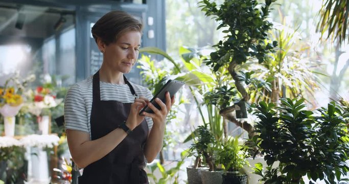 Young entrepreneur touching tablet screen looking at flowers in florist's shop enjoying nature and modern technology. People, entrepreneurship and business concept.