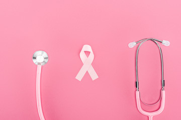 Obraz na płótnie Canvas top view of stethoscope and pink breast cancer symbol on pink background