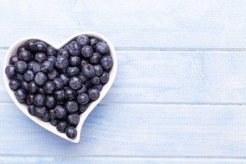 Fresh blueberries, in a heart shaped bowl on a wooden background.