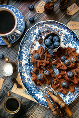 Overhead shot of homemade yummy chocolate waffles on vintage plates with blue ornament stands on wooden dark table