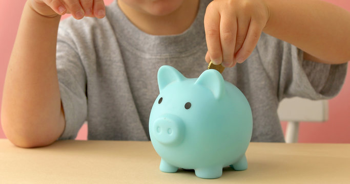 Little boy puts coins and shakes piggy bank at home