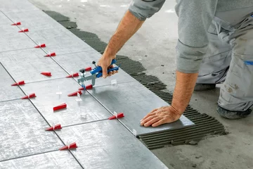 Fotobehang Ceramic Tiles. Tiler placing ceramic wall tile in position over adhesive with lash tile leveling system - Image © cnikola