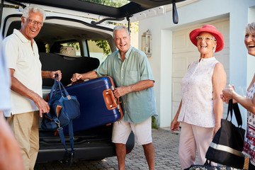 Group Of Senior Friends Loading Luggage Into Trunk Of Car About To Leave For Vacation