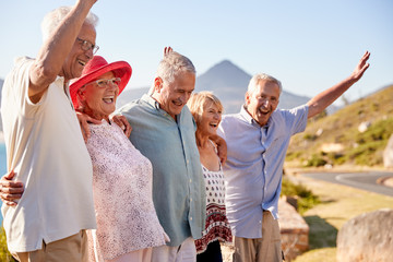 Senior Friends Visiting Tourist Landmark On Group Vacation With Arms Raised - Powered by Adobe