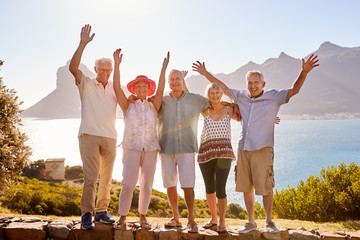 Portrait Of Senior Friends Visiting Tourist Landmark On Group Vacation With Arms Raised