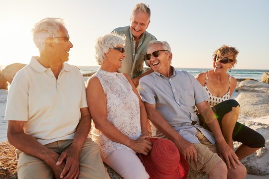 Group Of Senior Friends Sitting On Rocks By Sea On Summer Group Vacation