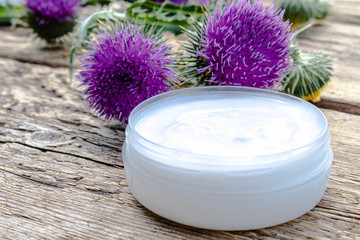 Obraz na płótnie Canvas Cream with flowers thistle on wooden background. Medicinal plant.