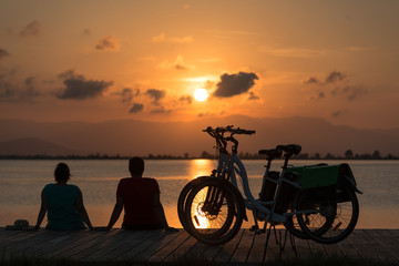 A couple enjoying the sunset seated in the dock next to two parked bicycles