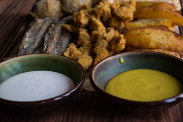 Fried potatoes with fish, cheese sticks and sauces.
