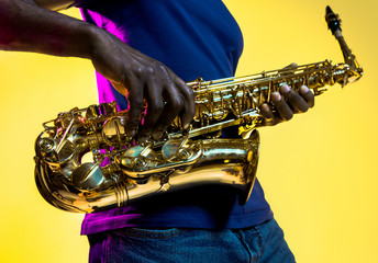 Young african-american jazz musician playing the saxophone on yellow studio background in trendy...