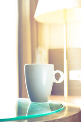 one cup hot coffee with smoke on the glass table in the window light in room