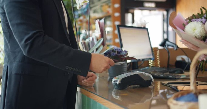 Slow motion of customer paying with bank card then taking bouquet of flowers from female florist in floral store. Business, people and technology concept.
