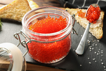 Composition with caviar in glass jar, bread, spoon, towel and cutting board, space for text