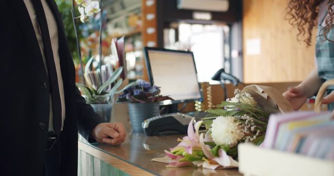 Man purchasing flowers paying with cash dollars in florist's store giving money to cashier taking bouquet from saleswoman. Commerce, business and people concept.