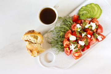 Breakfast salad with tomatoes, avocado, bun, pea sprouts, and coffee