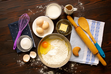 Wooden tabletop with set of products (flour, eggs, butter, sugar, vegetable oil, milk) and tools, needed for baking. Warm shot. Flat lay.