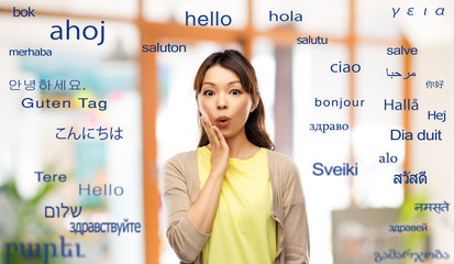 translation, education and people concept - surprised asian woman over greeting words in different...
