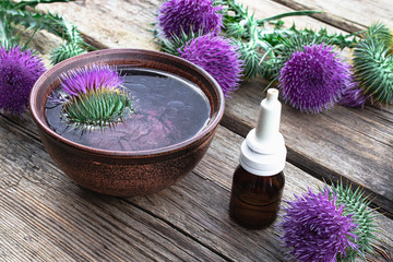 Obraz na płótnie Canvas Thistle essential oil in a bottle on the table near the thistle flowers on wooden background.
