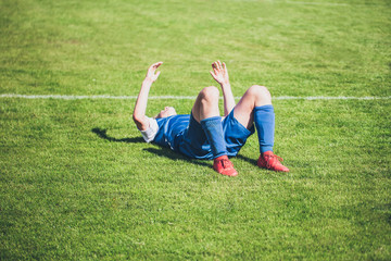 Fototapeta na wymiar Football player lying on the lawn from the annoyance of a miss on goal - emotions on the football field during the game - excitement