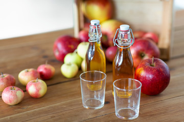 fruits, food and harvest concept - two glasses and bottles of apple juice or cider on wooden table