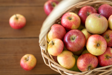 fruits, food and harvest concept - ripe apples in wicker basket on wooden table