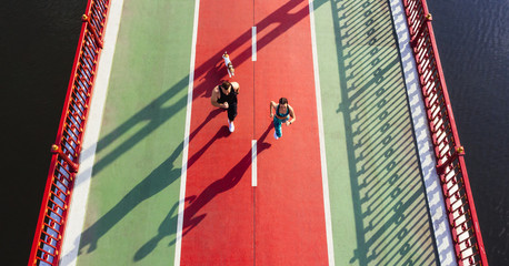Couple with dog running marathon on green and red bridge. Time for sport. Healthy vibes lifestyle. Aerial drone top view