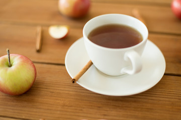 objects and drinks concept - cup of black tea with apples and cinnamon on wooden table