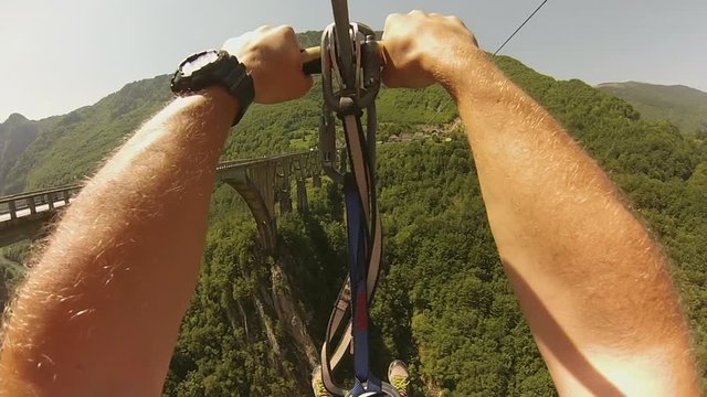 The traveling young man has an extreme vacation in high mountains, going on a rope over the canyon with mountain river. Zip-line. A tourist, traveler, explorer, outdoor adventure and tourism.
