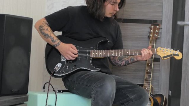 Young male with tattoo play on electro guitar 