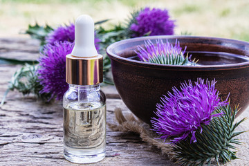 Obraz na płótnie Canvas A bottle of tincture or potion's essential oil and flowers of thistle on a wooden background.