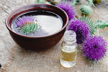 Obraz na płótnie Canvas A bottle of tincture or potion's essential oil and flowers of thistle on a wooden background