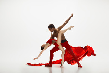 Graceful classic ballet dancers dancing isolated on white studio background. Couple in bright red clothes like a combination of wine and milk. The grace, artist, movement, action and motion concept.