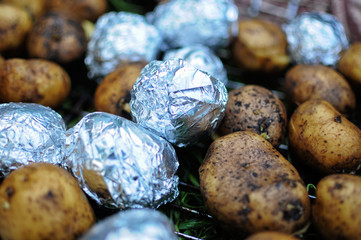 Baked potatoes wrapped in aluminum foil for baking. Some potatoes without foil.