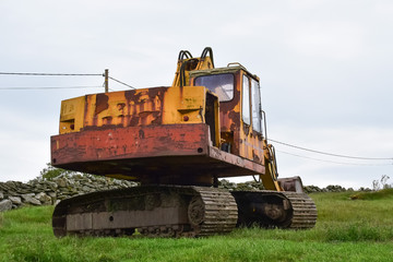 Big yellow excavator on a green hill near a stone fence. Concept: Road and construction work.