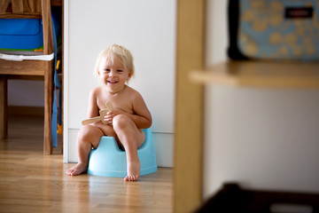 Little toddler boy, sitting on potty, playing with wooden toy