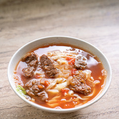 Beef noodle ramen meal with tomato sauce broth in bowl on bright wooden table, famous chinese style food in Taiwan, close up, top view, copy space